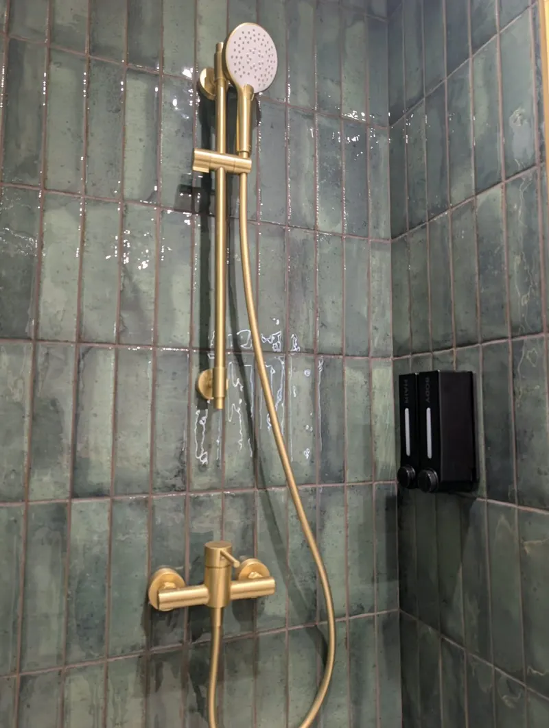 Douche aux carreaux verts et robinetterie laiton, propre et brillante